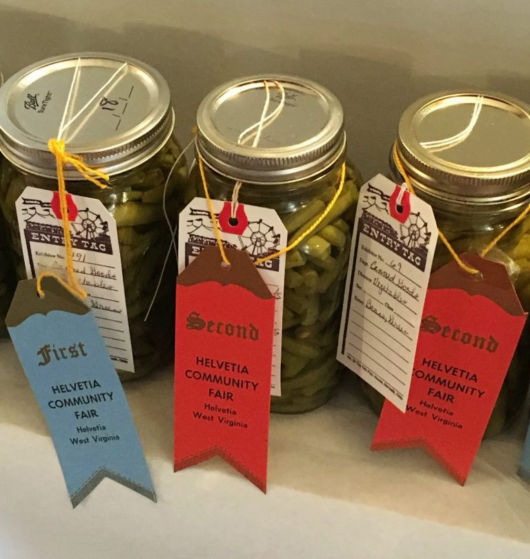 Mason jars of preserved foods with first, second, and third place ribbons from community fair