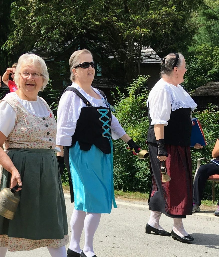 Three women in traditional Swiss-German dress carry bells in Helvetia Community Fair Alpine parade.