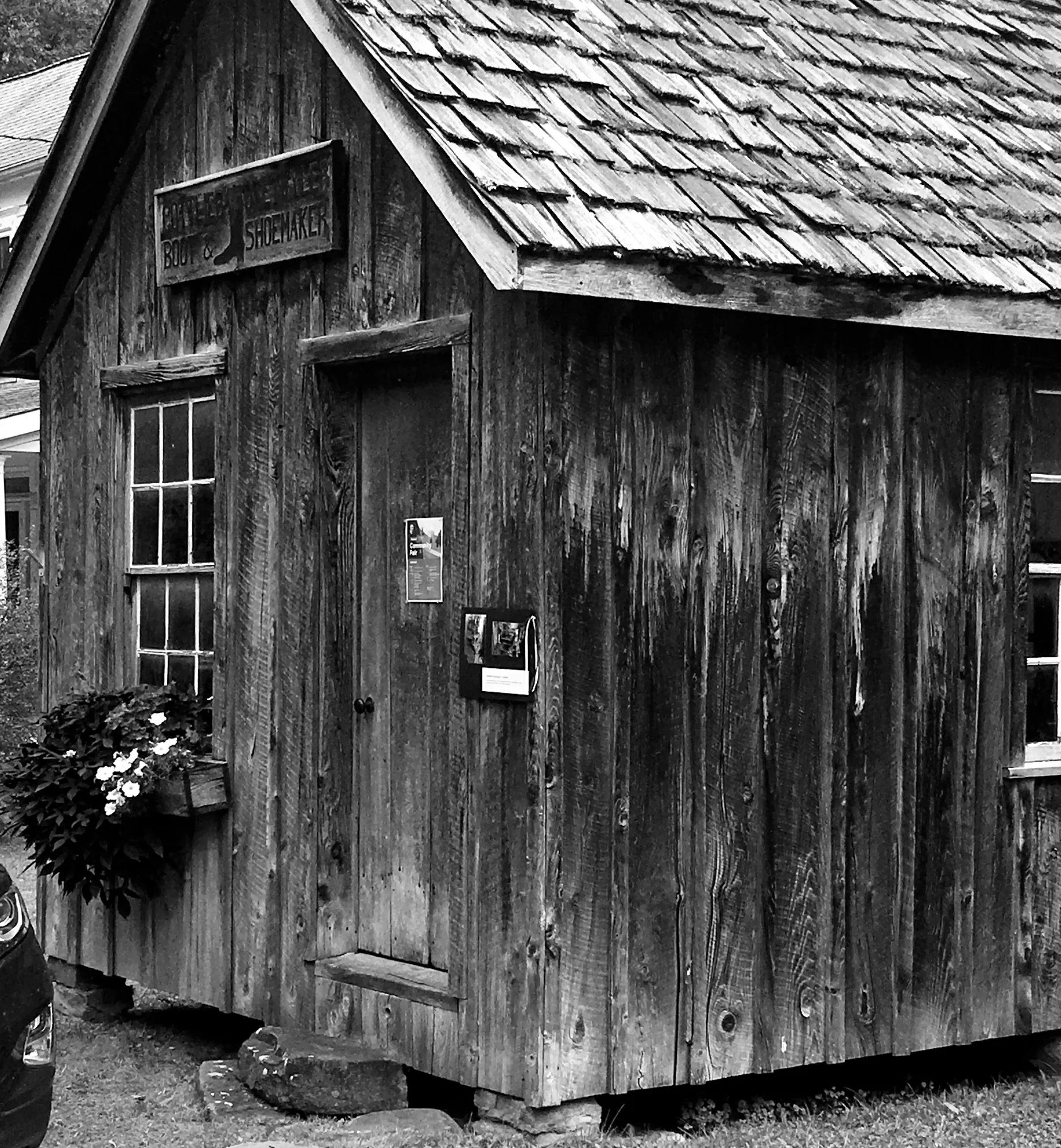 Historic weathered wooden building labeled Boot and Shoemaker in black and white