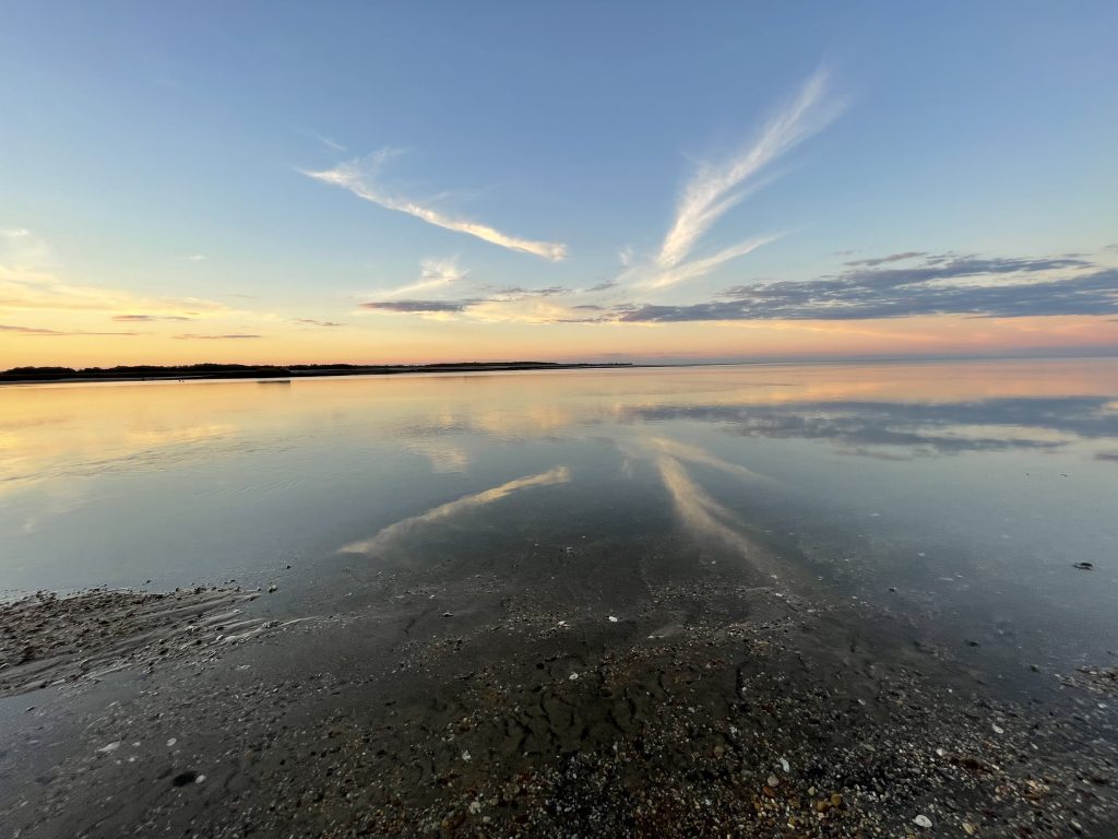 contrails reflect in the still water of the bay at sunset.