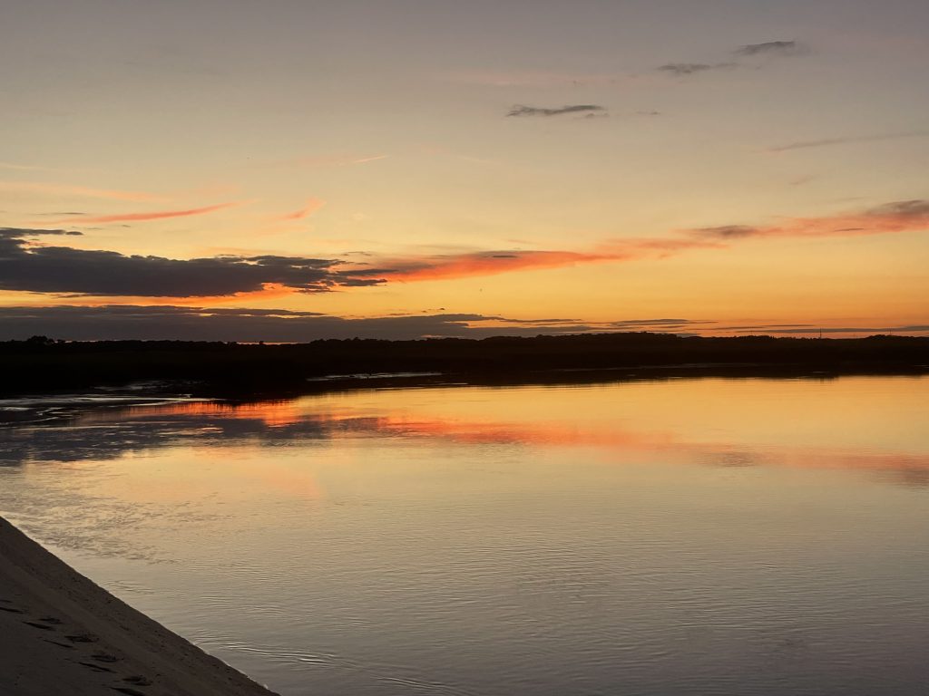 Orange and gold clouds reflect on calm waters.